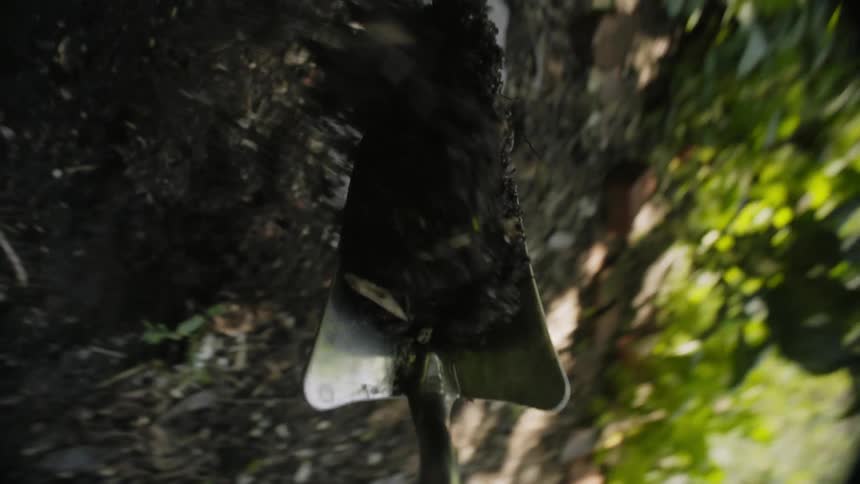 POV of a small metal trowel digging a hole and making a pile of dirt