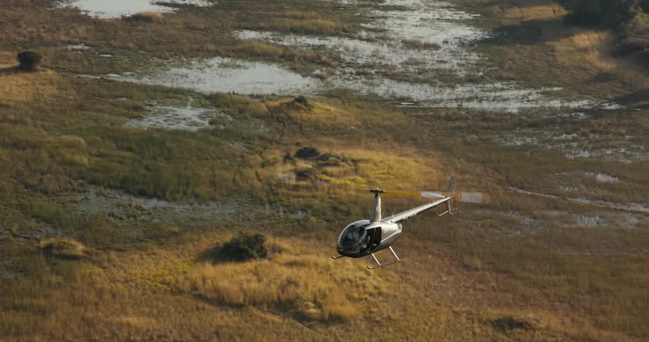 A helicopter hovers over a savanna and marshy area