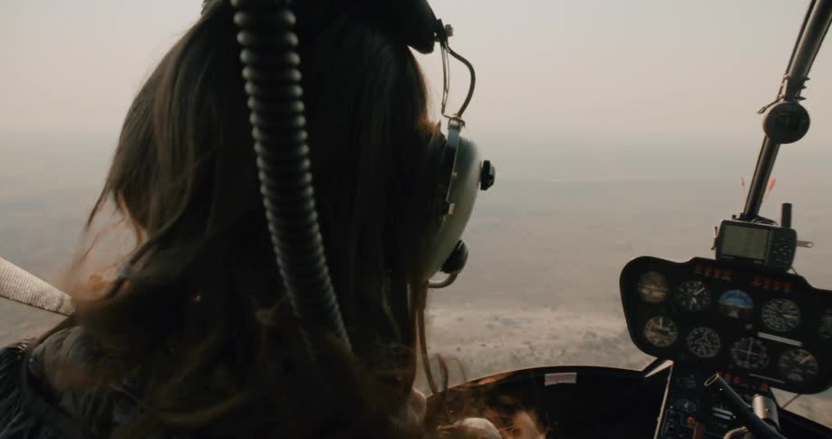 Woman in a cockpit of a helicopter that is flying above a natural environment