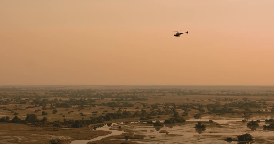Aerial view of a helicopter flying above a jungle in a reddish sky