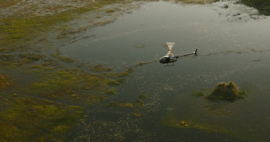 A black helicopter flying over a swamp with lots of green vegetation on the Okavango Delta