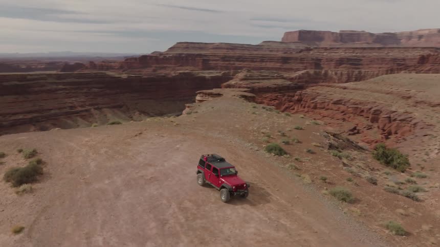 A red offroad car is driving in a desert with some canyons