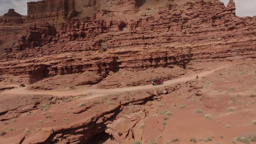 A red off road vehicle navigating a winding dirt road amidst large red rock formations