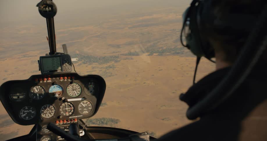 Person in a helicopter cockpit flying over a natural environment