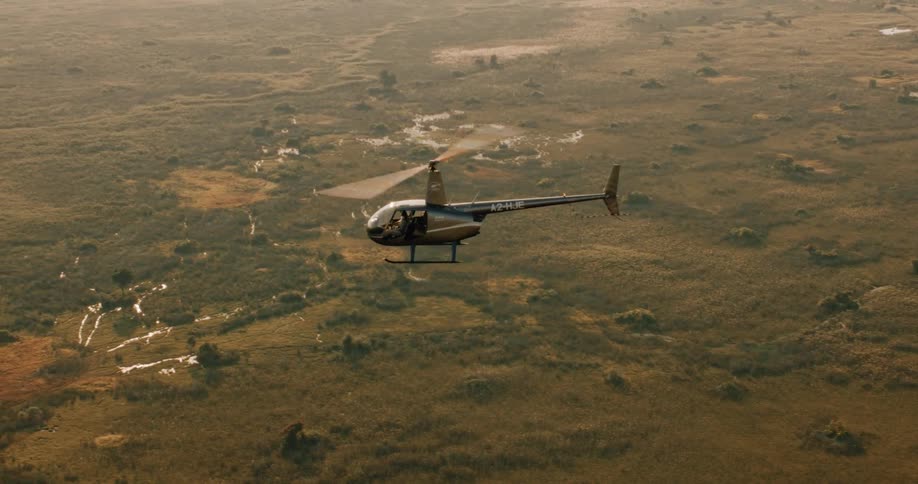 A black helicopter flying over a green field with streams