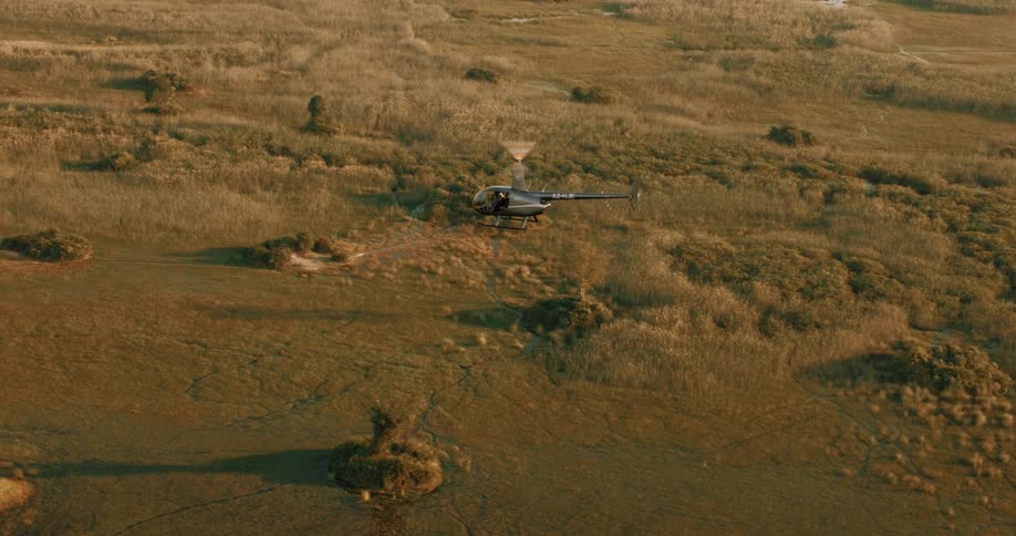 A helicopter flies over a vast savanna
