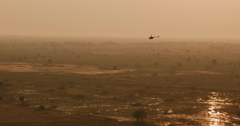Helicopter flies through the hazy sky over wetlands surrounded by grasslands