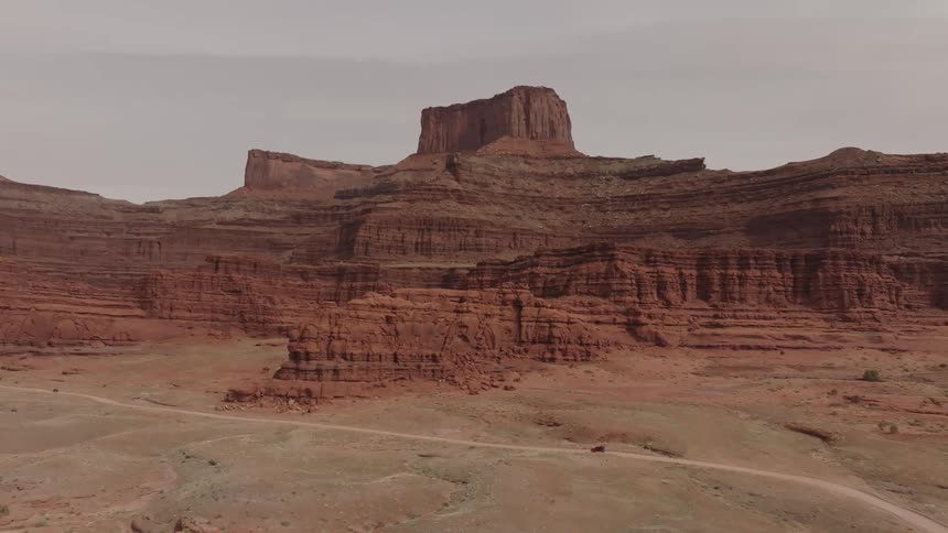 A vehicle drives on a road through a desert next to a stunning mountain cut away by glaciers