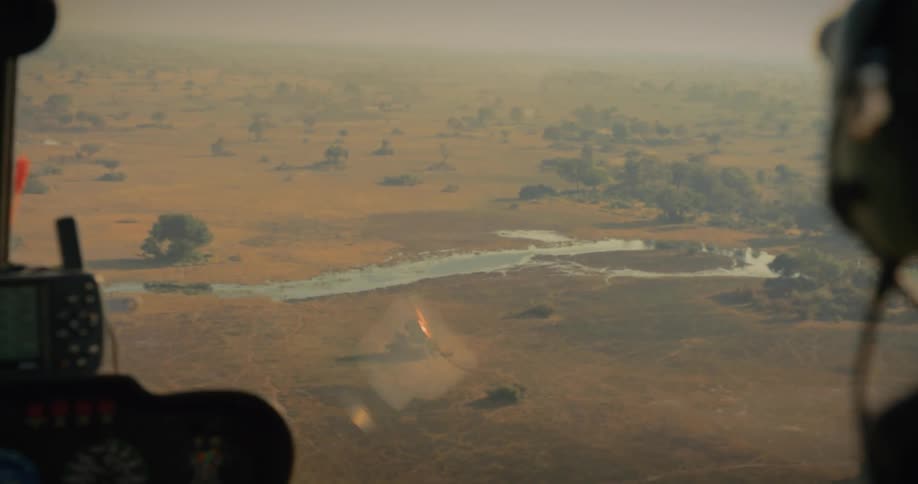 A view from inside a helicopter of a savannah with a river and some trees