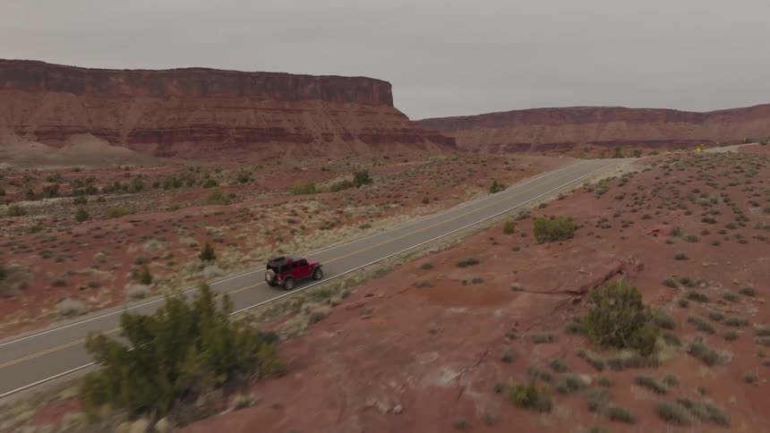 Red jeep traveling on a paved road in a natural environment surrounded by canyons