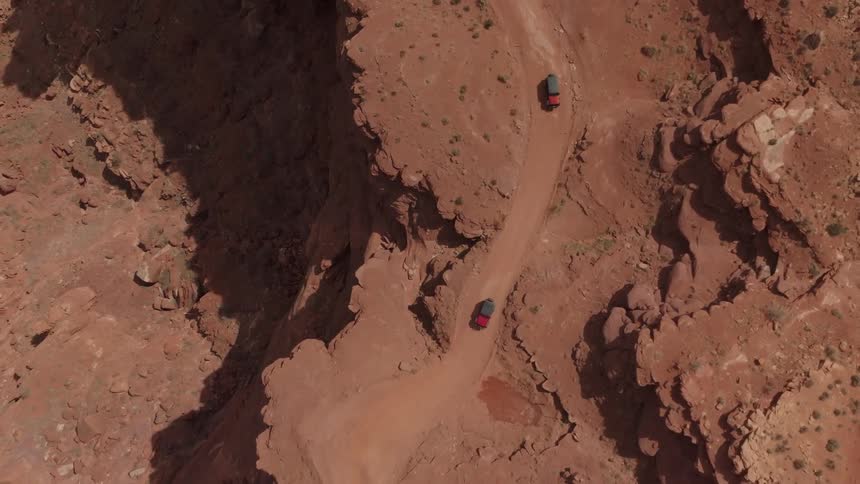 Aerial view of two red vehicles traveling along winding roads in canyons
