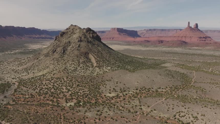 A desert region with a high land formation and in the background there are mountains and canyons