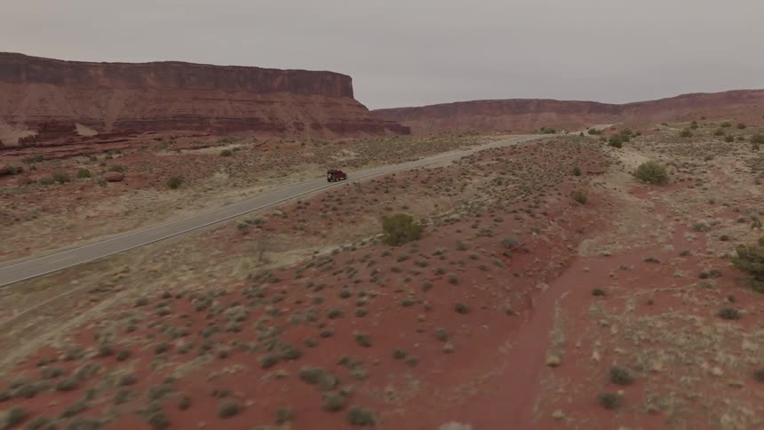 A vehicle drives down a remote road that runs through a desert area