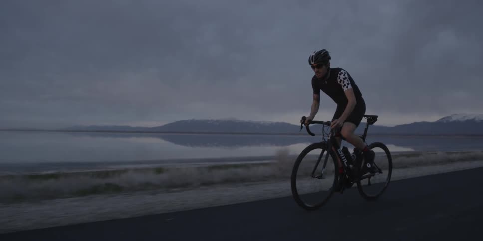 Bicyclist riding along a large lake on a very cloudy day