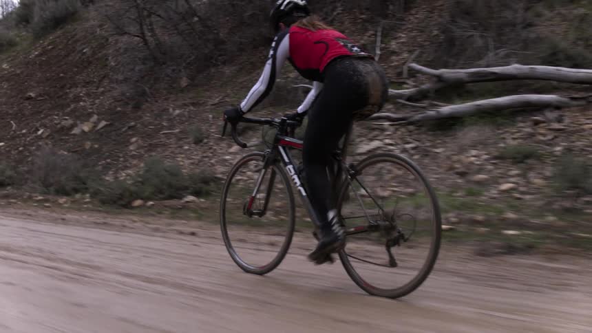 Bicyclist pedaling up a small incline on a wet dirt road