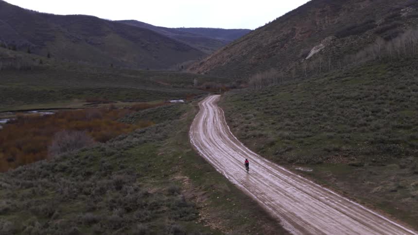 A person rides a bike along a muddy dirt road in the foothills