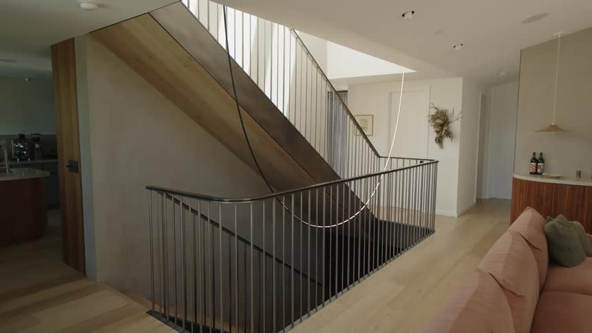 The interior of a house with a wooden floor and two levels of staircase with black handrails