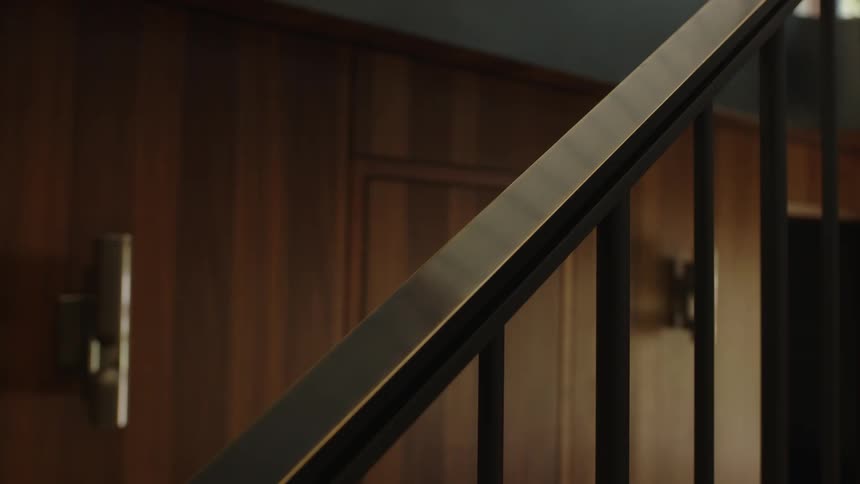 A closeup of a darktoned staircase railing with a metallic finish against a rich wooden wall