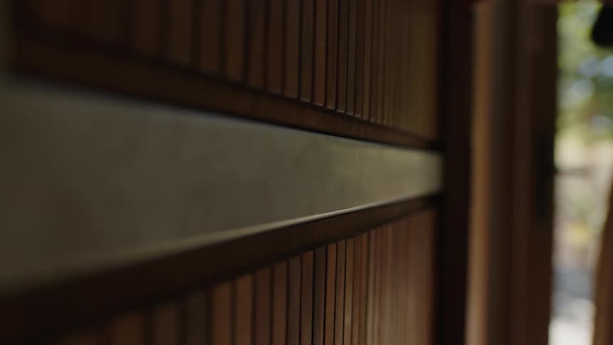 A wooden wall with a white stripe in the middle and behind there is a person opening a door