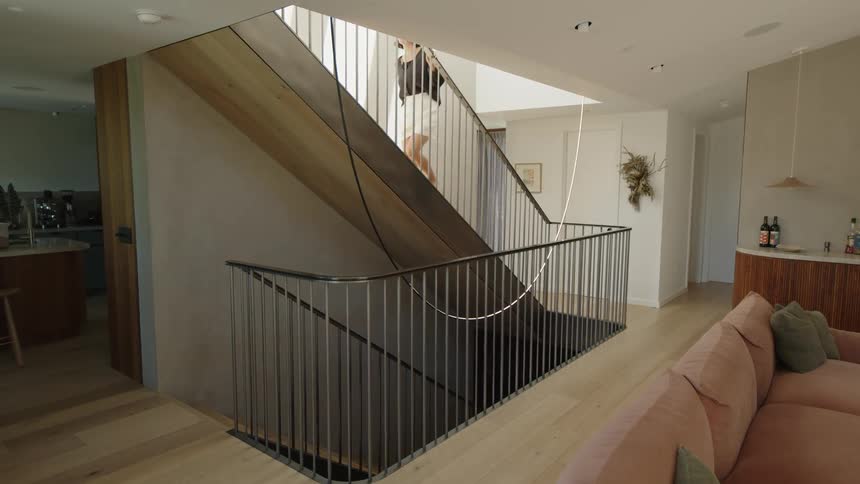 Interior design of a living room and in the background a woman walking up the stairs of the house