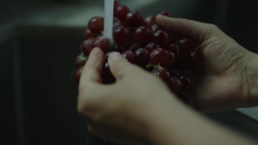 Human hands holding a bunch of grapes washing them in water from a tap