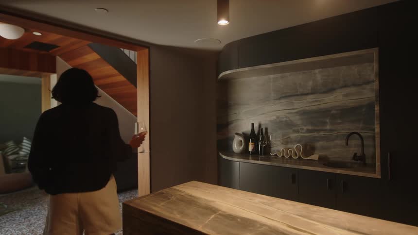 Woman picking up a glass of wine on a wooden countertop and walking around the house