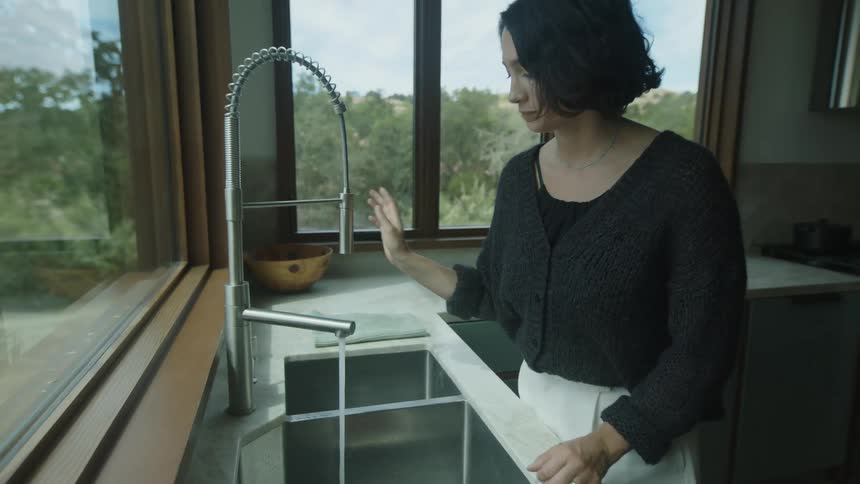 Woman in the kitchen turning on the sink tap