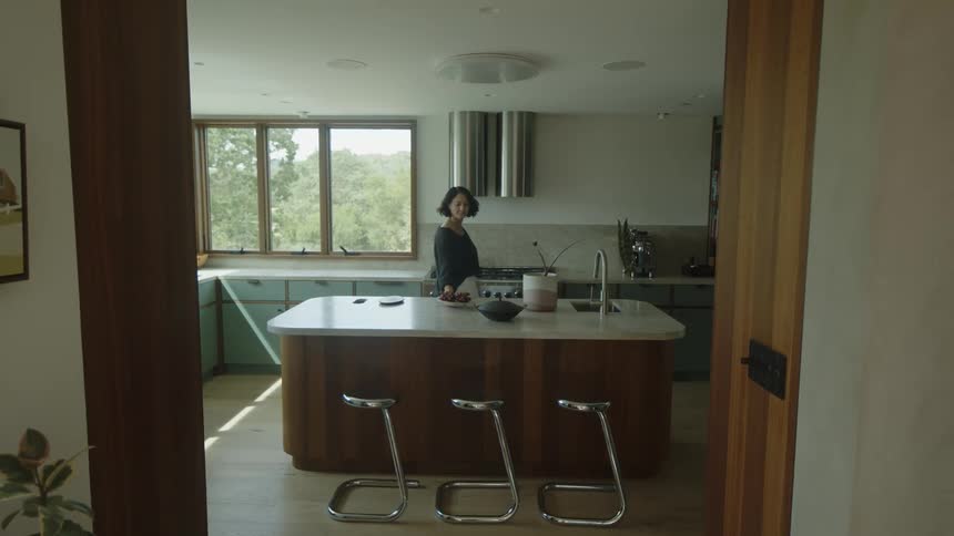 A woman in a kitchen places a bowl of fruit on a countertop
