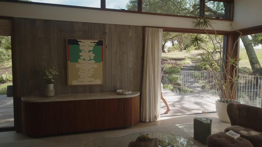 A woman opens a large glass door leading to an outdoors area in a modern house