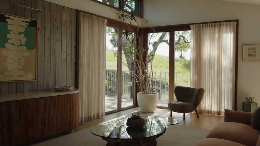 A cozy living room with large windows light curtains and modern furniture overlooks a scenic outdoor view