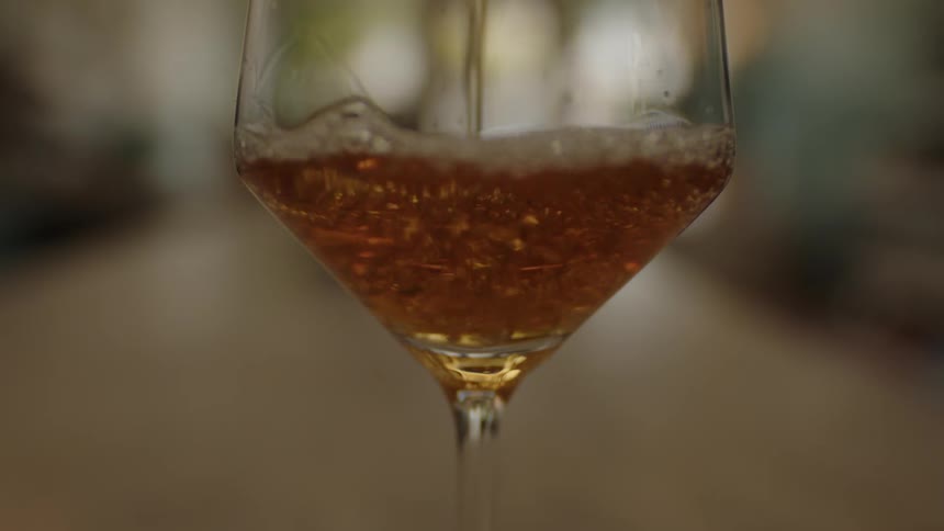 A closeup shows a wine glass being slowly filled with light red colored wine