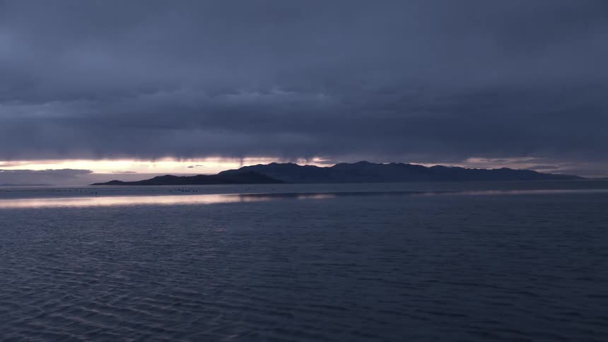 A view of the ocean with mountains and stormy skies in the background