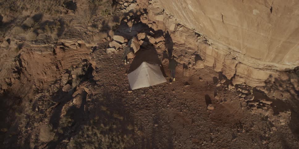 A man walks towards a tent near a cliffside