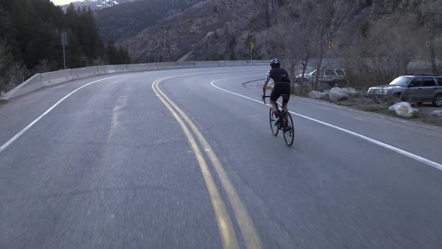 A man furiously peddles his bike around a turning road