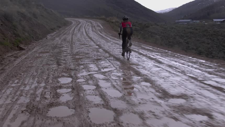 A bicyclist rides on a muddy rural road