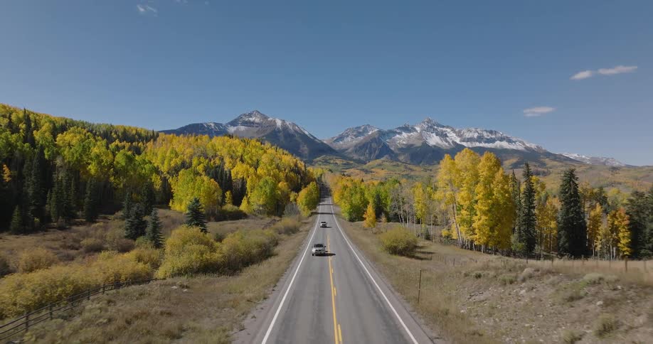 Aerial landscape of a highway with vehicle traffic surrounded by conifers and snowy mountains on the horizon