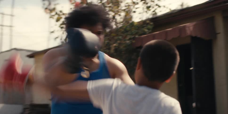 Man and boy wearing boxing gloves and spar in a backyard