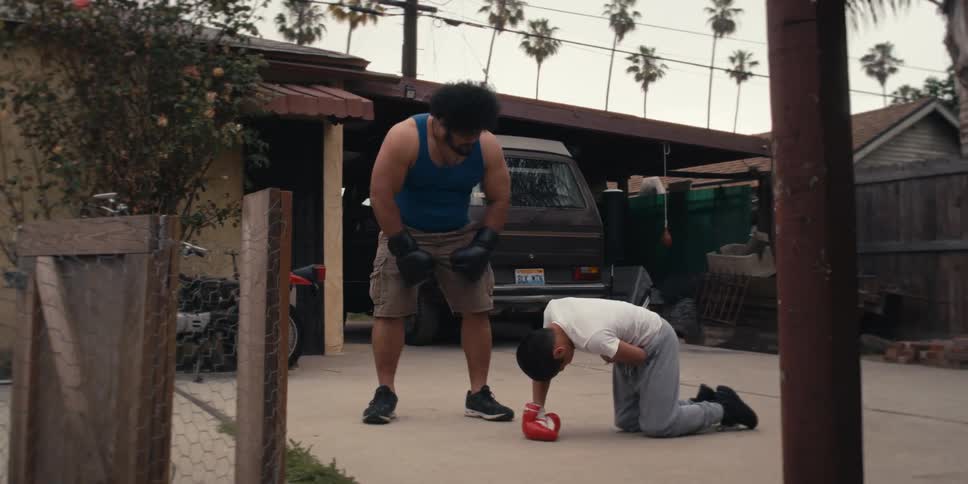 Man crouching down and checking on a boy who has one hand on his stomach while both are wearing boxing gloves
