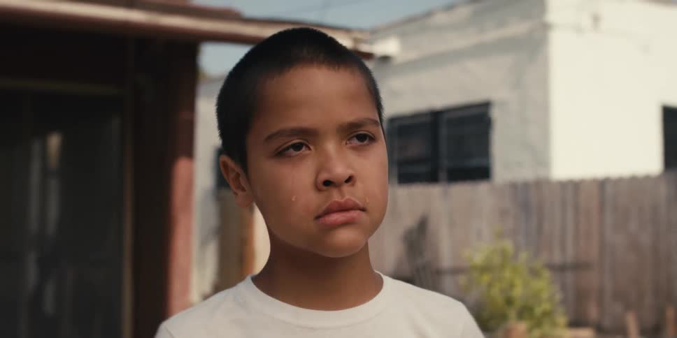 A tear runs down the cheek of a boy standing in the backyard