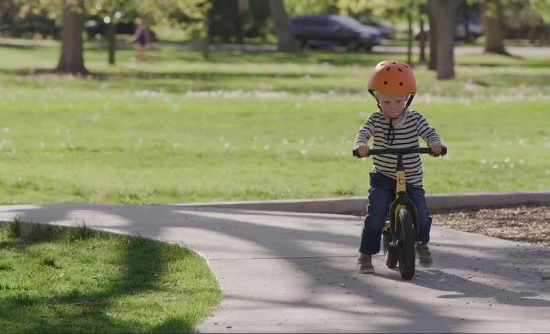 Small boy in an orange helmet riding a bicycle in a park