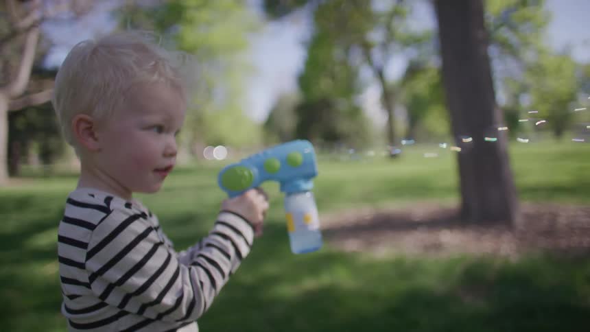 Small blond boy holding a toy that blows soap bubbles in an outdoor environment