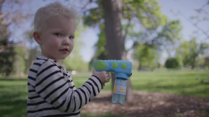 A child in a striped shirt holds a toy bubble gun outdoors