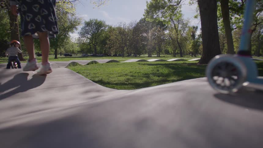Children ride on skates bicycle and scooter through a park with hilly sidewalks