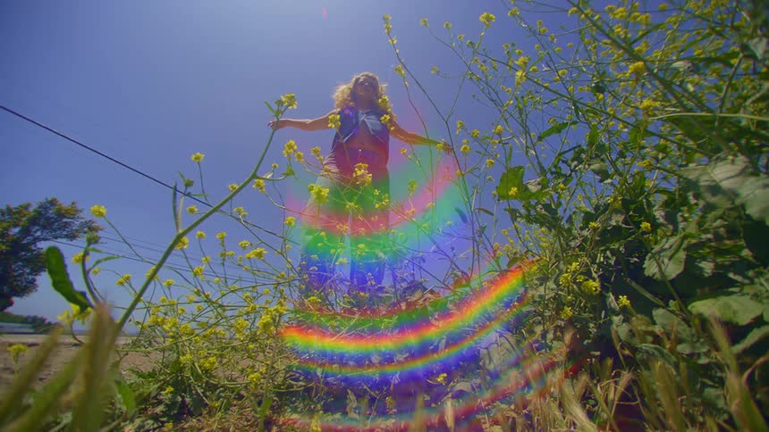 A woman raises her arms near a rainbow