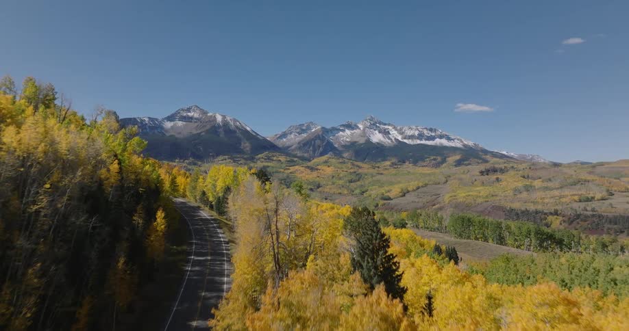 Aerial view of a scenic landscape a mountain range and a forest with yellow foliage a road cuts through the forest