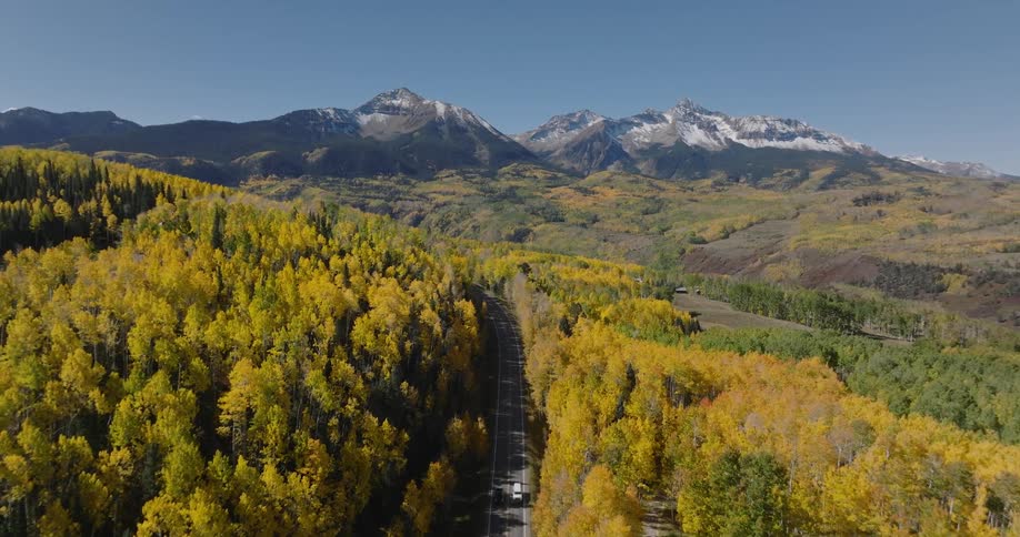 Aerial view of a scenic landscape a mountain range and a forest with yellow foliage with a road cutting through the forest