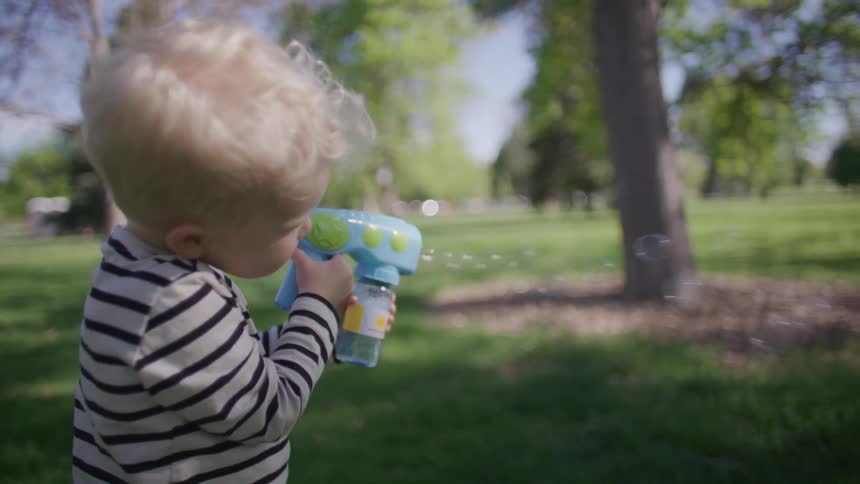 A young boy is playing with a bubble gun in a park on a spring day
