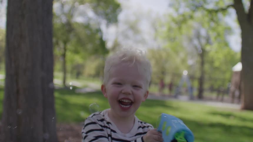 Little boy running around having fun while using a toy gun that releases soap bubbles