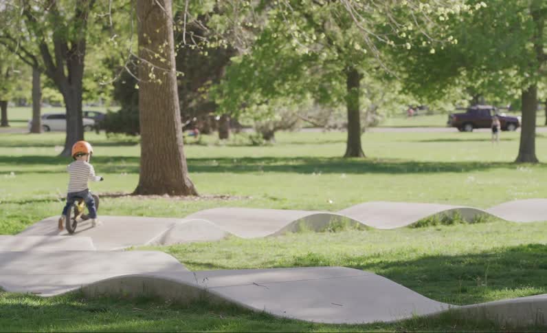Little boy riding a bicycle with a helmet on a raised track in a park during the day