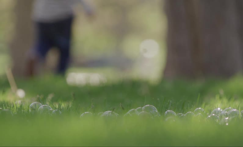 Closeup on green grass with soap bubbles and the silhouette of children running in the background